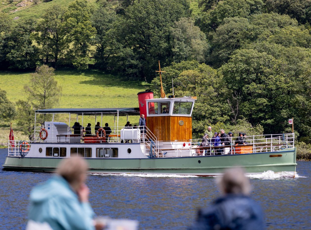 Two walkers watch on as an Ullswater Steamer cruises by on Ullswater Lake